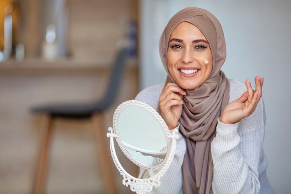 0 Muslim woman applying cream to face and looking to mirror